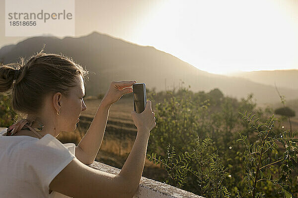 Frau fotografiert bei Sonnenuntergang mit Smartphone