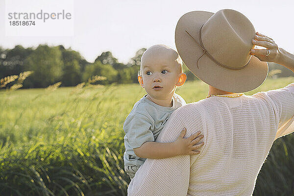 Mother wearing hat carrying son in nature on sunny day
