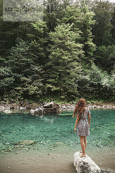 Junge Frau steht auf einem Felsen vor dem Fluss