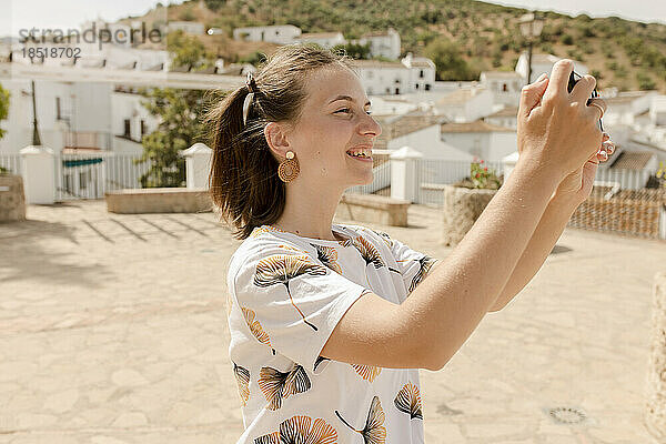 Glückliche junge Frau  die an einem sonnigen Tag mit dem Handy fotografiert