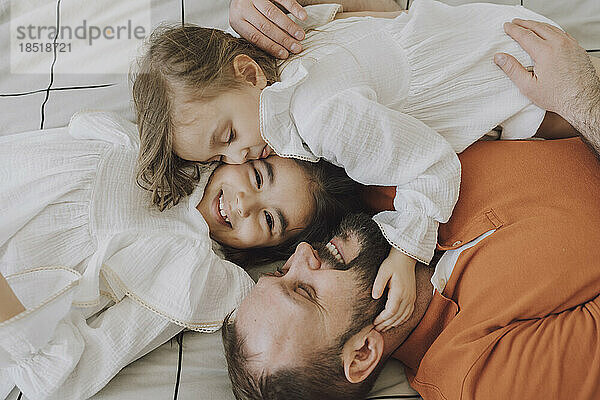 Glücklicher Vater umarmt süße Töchter zu Hause im Bett