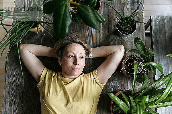 Thoughtful woman with hands behind head lying down amidst plants at home