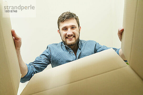 Glücklicher Mann packt Karton im neuen Zuhause aus