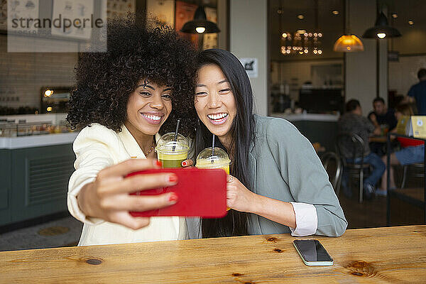 Fröhliche Freunde genießen Saft und machen gemeinsam im Café ein Selfie