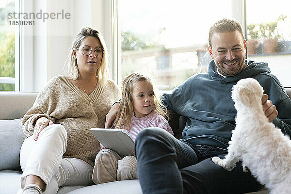 Glückliche Familie spielt mit Hund  der zu Hause auf dem Sofa sitzt