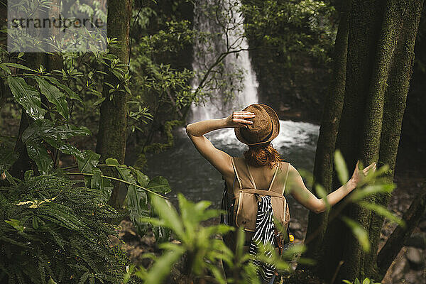 Junge Frau mit Hut steht vor Wasserfall