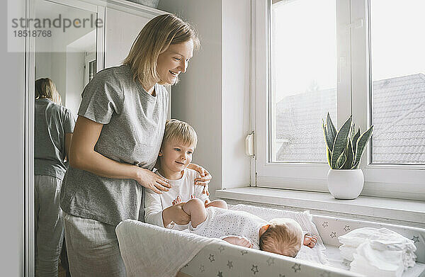 Happy woman looking at boy taking care of brother at home