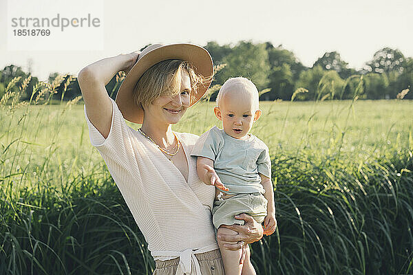 Happy mother wearing hat carrying son in nature on sunny day