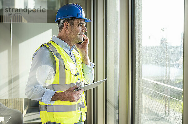 Lächelnder Ingenieur mit Tablet-PC  der im Büro auf dem Smartphone spricht