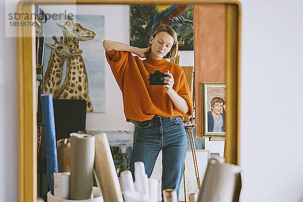 Spiegelbild einer Frau  die im Kunstatelier eine Kamera am Spiegel hält
