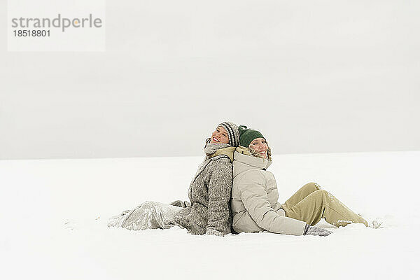 Glückliche Freunde sitzen im Winter im Schnee
