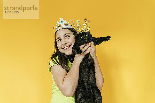 Glückliches Mädchen und Katze mit Krone vor gelbem Hintergrund