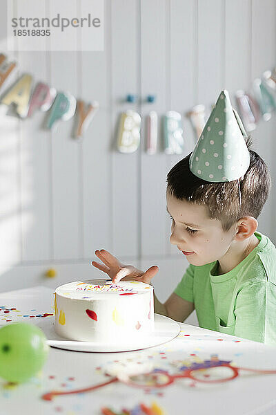 Junge berührt Geburtstagstorte auf Tisch zu Hause