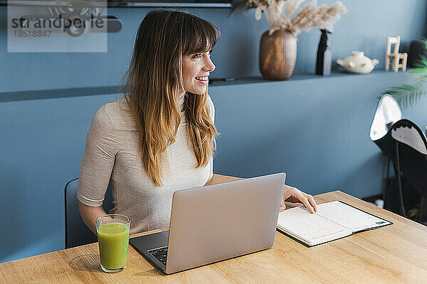 Lächelnder Freiberufler mit Laptop am Schreibtisch im Heimbüro