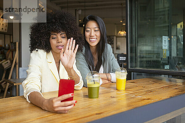 Frauen machen Videoanrufe auf Smartphones und sitzen im Café
