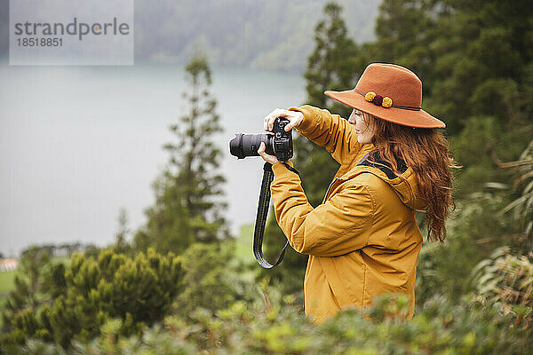 Rothaarige Frau mit Hut fotografiert mit der Kamera im Wald