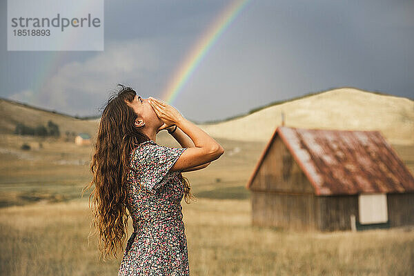 Optische Täuschung eines Regenbogens  der aus dem Mund einer Frau kommt  die auf dem Feld steht