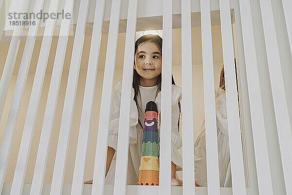 Girl with toy looking through striped railing at home
