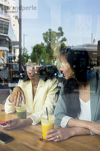 Freunde reden miteinander und sitzen im Café  gesehen durch das Fenster