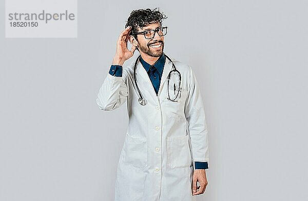 Lächelnder Arzt  der sich ein Gerücht anhört. Junger Arzt lächelnd mit Hand über Ohr isoliert  Lächelnder Arzt streckt Hand isoliert