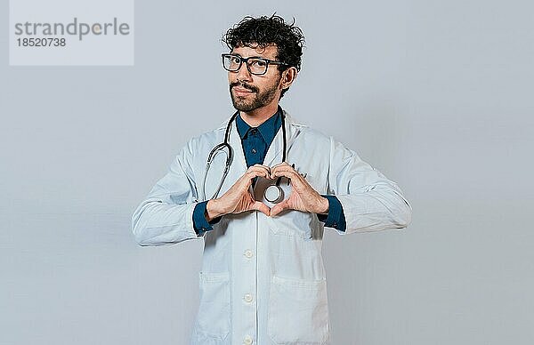 Handsome Arzt macht Herz Geste mit den Händen. Glücklicher Arzt zeigt mit den Fingern nach unten  junger Arzt macht Herzform isoliert