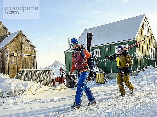 Skibergsteiger tragen ihre Ski durch Tasiilaq im Winter  Insel Ammassalik  Kommuneqarfik Sermersooq  Ostgrönland  Grönland  Nordamerika