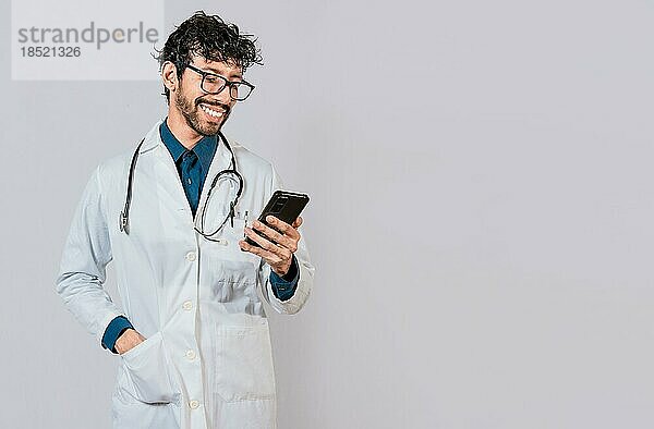 Junger Arzt mit Telefon isoliert  Glücklicher Arzt mit Telefon auf isoliertem Hintergrund. Lächelnder Arzt mit Handy isoliert