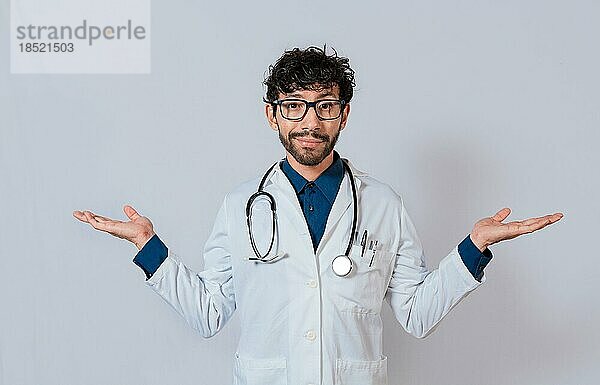 Arzt präsentiert etwas mit beiden Handflächen. Junger Arzt mit seitlich geöffneten Handflächen. Bärtiger Arzt mit beiden geöffneten Handflächen