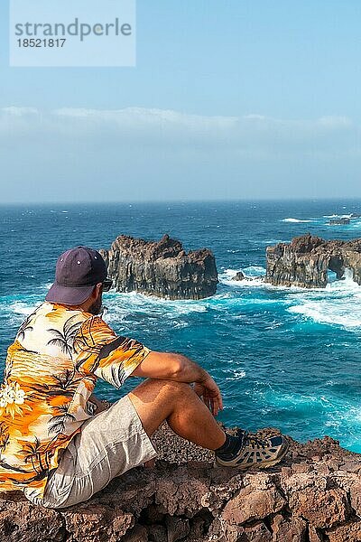 Insel El Hierro. Kanarische Inseln  Tourist Mann in den Bogen von La Tosca sitzen. Denkmal an der Küste