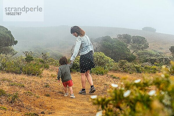 Mutter und Sohn spazieren mit Blumen zu einem vom Wind verdrehten Sabinar Baum auf El Hierro. Kanarische Inseln
