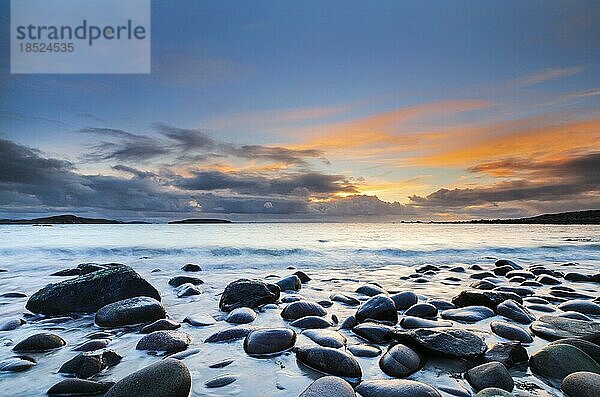 Orange farbiger Wolkenhimmel bei Sonnenuntergang an einem mit runden Steinen besäten Srand bei Achiltibuie an der Westküste Schottlands