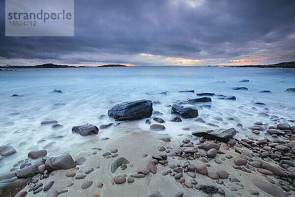 Drammatischer Wolkenhimmel bei Sonnenuntergang an einem mit runden Steinen besäten Sandstrand bei Achiltibuie an der Westküste Schottlands