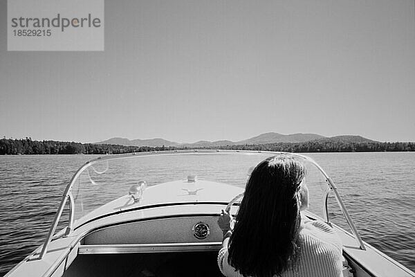 Vereinigte Staaten  New York  Santa Clara  Rückansicht einer Frau  die ein Motorboot auf dem Upper Saranac Lake fährt  schwarz und weiß