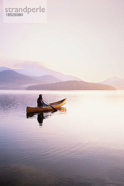 Vereinigte Staaten  New York  Frau paddelt Kanu auf Lake Placid bei Sonnenaufgang  Adirondacks State Park