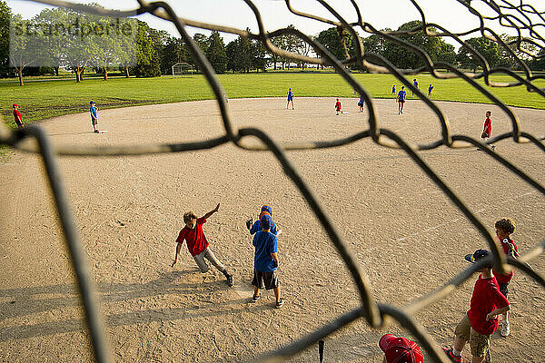 Ein Junge im Grundschulalter rutscht während eines T-Ball-Spiels nach Hause  während seine Mannschaftskameraden dahinter stehen und zusehen; Lincoln  Nebraska  Vereinigte Staaten von Amerika