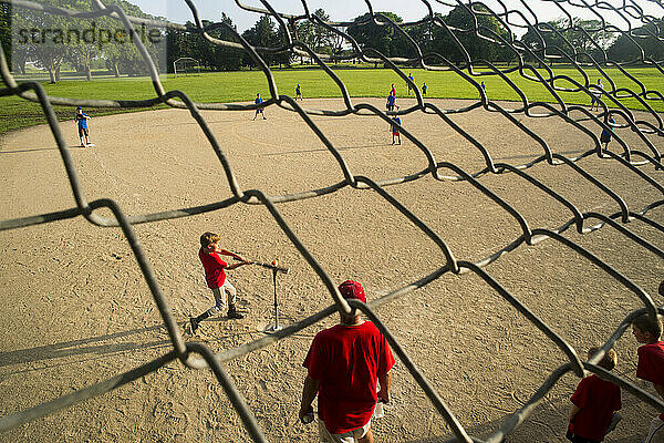 Ein Junge im Grundschulalter tritt während eines T-Ball-Spiels auf das Schlagmal  während sein Trainer und seine Mannschaftskameraden hinter ihm stehen und zusehen; Lincoln  Nebraska  Vereinigte Staaten von Amerika