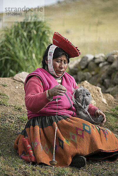 Frau sitzt auf einem grasbewachsenen Hügel und arbeitet an einer traditionellen Handweberei; Cusco  Peru