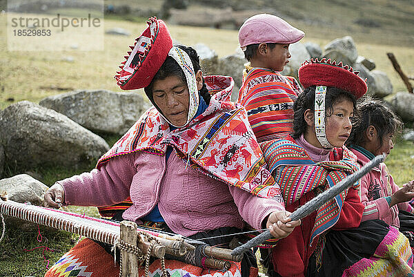 Frau sitzt bei der Arbeit an einer traditionellen Handweberei  mit Kindern an ihrer Seite; Cusco  Peru