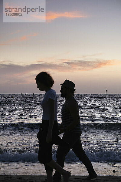 Silhouettiertes Paar  das bei Sonnenuntergang am Strand spazieren geht; Melbourne  Victoria  Australien