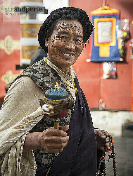 Tibetischer Mann in traditioneller Kleidung  der eine Gebetsmühle hält; Lhasa  Tibet