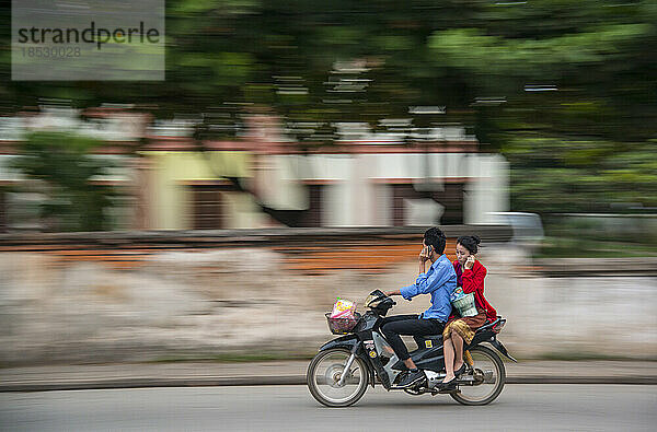 Motorradfahrer und sein Fahrer telefonieren während der Fahrt mit einem Handy; Luang Prabang  Laos