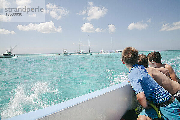 Drei Jungen blicken von einem Boot aus in Richtung Stingray City  einer beliebten vorgelagerten Sandbank  auf der sich die Rochen an den Menschen gewöhnt haben  so dass sie gefahrlos neben den Tieren schwimmen können; Grand Cayman  Cayman Islands