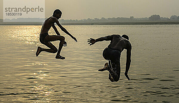 Zwei Jungen springen bei Sonnenaufgang in den Ganges; Varanasi  Indien