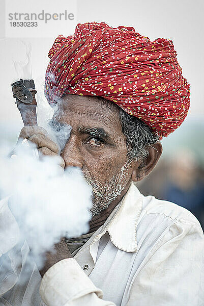 Nahaufnahme eines indischen Mannes  der eine Chillum-Pfeife raucht und den Rauch aus dem Mund bläst; Pushkar  Rajasthan  Indien