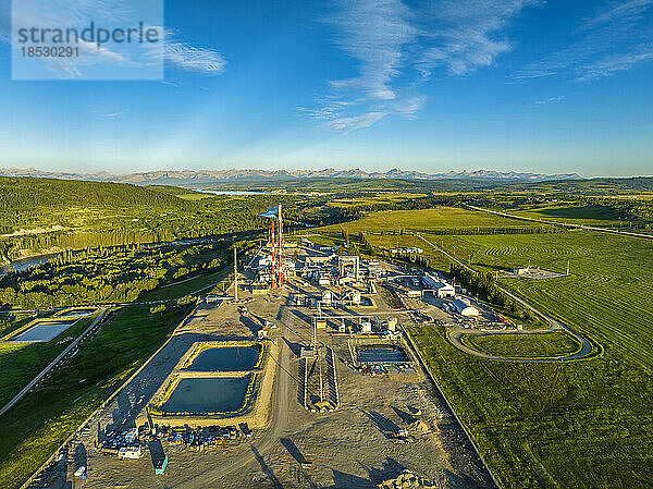 Luftaufnahme eines Gaswerks entlang eines Flusses mit blauem Himmel  Wolken und Bergen im Hintergrund  westlich von Cochrane  Alberta; Alberta  Kanada