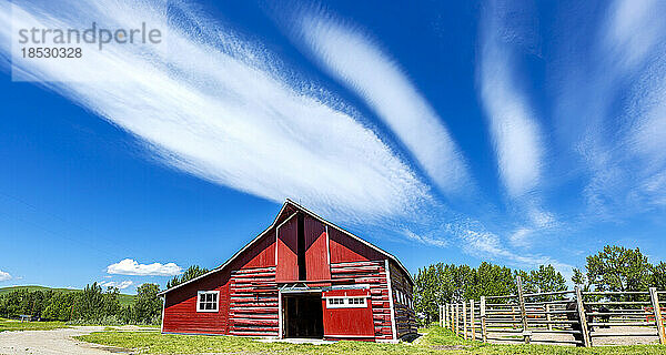 Historische rot gestrichene Scheune mit Holzzaun und dramatischen Wolken und blauem Himmel  südlich von Longview  Alberta; Alberta  Kanada