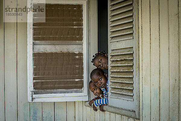 Drei Geschwister schauen aus dem Fenster ihres Hauses in der Unternehmensstadt Socapalm im Bezirk Kribi in Kamerun; Socapalm  Kribi  Kamerun