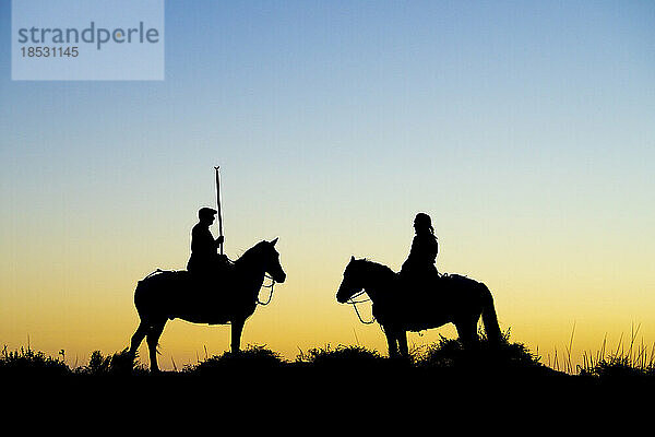 Reiter und ihre Pferde als Silhouette bei Sonnenaufgang; Saintes-Maries-de-la-Mer  Frankreich