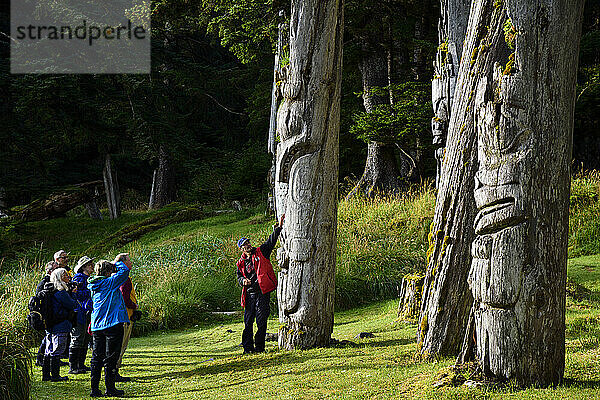 Touristen mit Führer bei der Besichtigung der Totempfähle in SGang Gwaay Llanagaay  Ninstints auf Englisch  einer verlassenen Haida-Dorfstätte auf Anthony Island; Anthony Island  Haida Gwaii  British Columbia  Kanada
