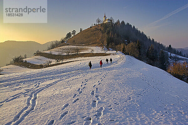 Slowenen wandern auf einem schneebedeckten Weg zu einer Kirche auf einem Hügel in der Nähe von Ljubljana; Slowenien